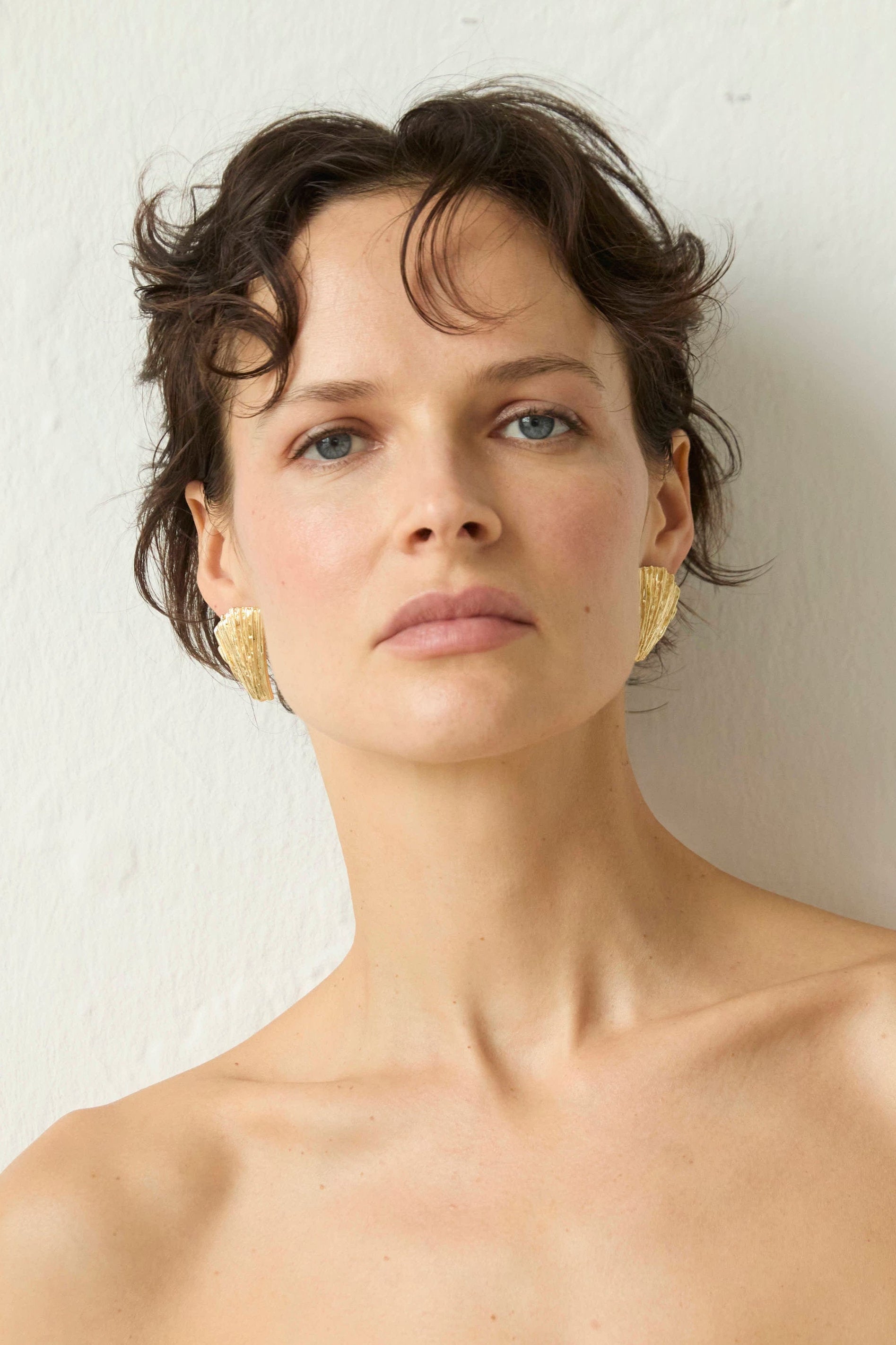 Woman with short hair wearing gold Neréa earrings against a plain background